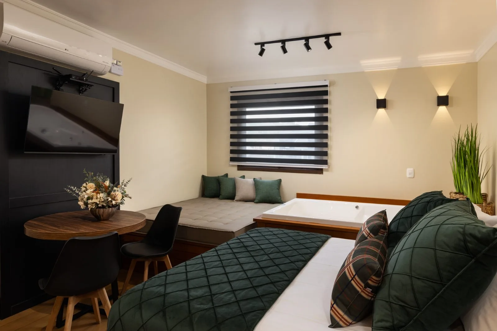 Suíte com banheira de hidromassagem, day bed, mesa de refeições e TV na parede