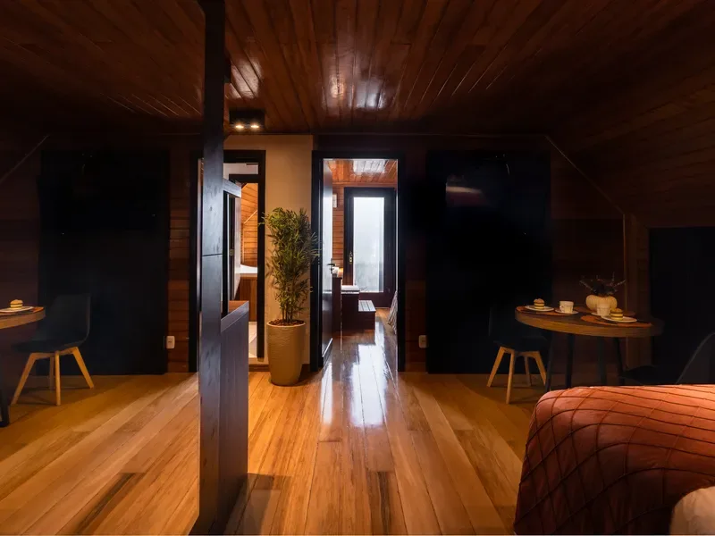 Corredor interno revestido de madeira, com portas escuras de acesso às suítes e uma passagem aberta ao fundo deixando entrar a luz